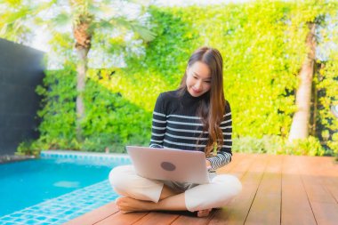 Genç Asyalı bir kadının portresi oteldeki yüzme havuzunda dizüstü bilgisayar kullanıyor.