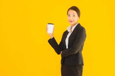 Portre güzel genç Asyalı kadın akıllı cep telefonu ve kahve fincanı ile izole edilmiş sarı arka planda