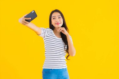 Güzel Asyalı genç bir kadının portresi mutlu bir gülümseme sarı izole edilmiş arka planda akıllı cep telefonu kullanın