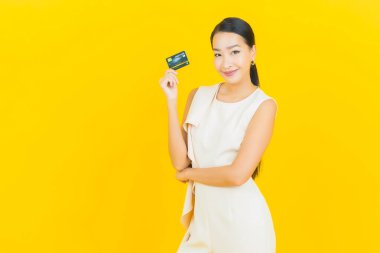 Asyalı güzel bir kadının portresi. Sarı arka planda kredi kartıyla gülümsüyor.