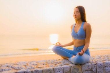 Genç Asyalı kadının portresi sağlık için gün doğumunda deniz kıyısı okyanusunda meditasyon yapıyor.
