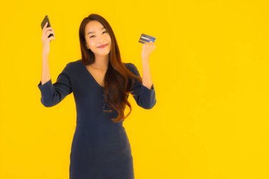 Akıllı cep telefonu, cep telefonu ve kredi kartı sarısı izole bir geçmişi olan güzel Asyalı bir kadın portresi.