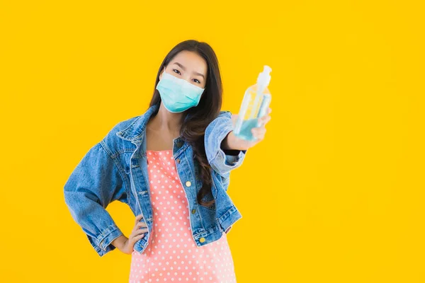 肖像画美しい若いアジアの女性は 黄色の隔離された背景にきれいにするためのアルコールジェルとコロナウイルスやCovid19を保護するためのマスクを着用 — ストック写真