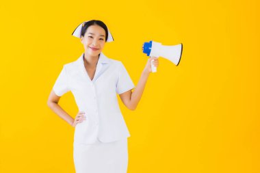 Asyalı güzel bir kadının portresi klinikte ve hastanede iletişim kurmak için megafonlu Taylandlı hemşire ve sarı izole bir arka plan.