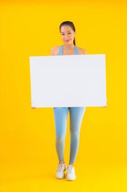 Güzel bir Asyalı kadın portresi spor giysisi giyer. Sarı izole edilmiş arka planda boş beyaz ilan panosu var.