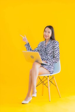 Güzel bir Asyalı kadın, sarı izole edilmiş arka planda dizüstü bilgisayar kullanıyor.