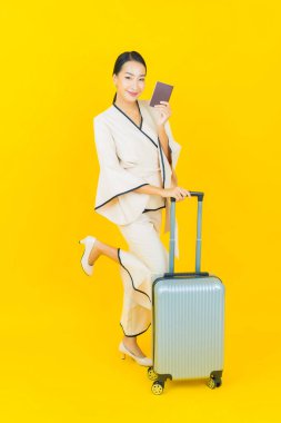Güzel, genç, iş kadını, bavul ve pasaportlu Asyalı kadın, sarı arka planda seyahat etmeye hazır.