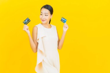 Asyalı güzel bir kadının portresi. Sarı arka planda kredi kartıyla gülümsüyor.