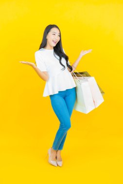 Sarı arka planda alışveriş çantasıyla gülümseyen güzel Asyalı kadın portresi