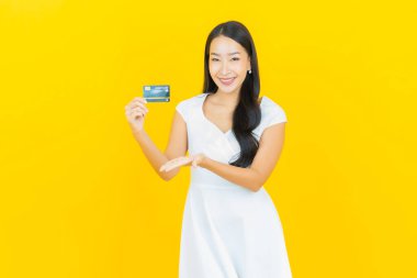 Asyalı güzel bir kadının portresi. Sarı arka planda kredi kartıyla gülümsüyor.