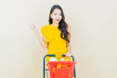 Renkli arka planda süpermarketten alınmış market sepetiyle gülümseyen güzel Asyalı kadın portresi.