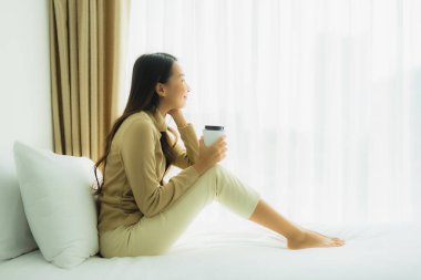 Yatak odasının iç tarafında, kahve fincanı olan Asyalı genç bir kadın.