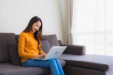 Genç Asyalı bir kadının oturma odasında çalışmak için dizüstü bilgisayar defteri kullanmasının portresi.
