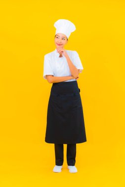 Güzel bir Asyalı kadın portresi ya da sarı izole arkaplanda şapkası olan aşçı üniforması.