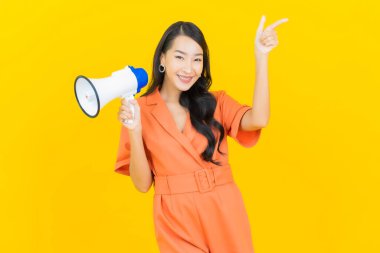 Asyalı güzel bir kadının portresi sarı arka planda megafonla gülümsüyor.
