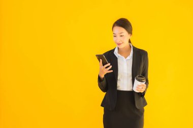 Portre güzel genç Asyalı kadın akıllı cep telefonu ve kahve fincanı ile izole edilmiş sarı arka planda