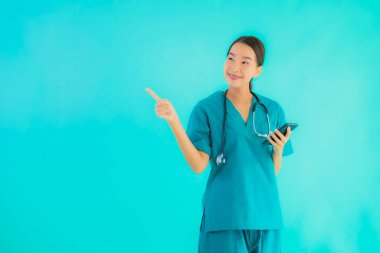 Güzel bir portre genç Asyalı doktor kadın mavi izole edilmiş arka planda akıllı cep telefonu gösteriyor.