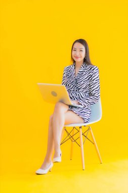 Güzel bir Asyalı kadın, sarı izole edilmiş arka planda dizüstü bilgisayar kullanıyor.