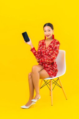 Güzel bir Asyalı kadın. Akıllı cep telefonu kullan. Sandalyeye otur.
