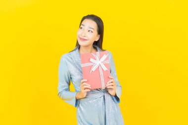 Asyalı güzel bir kadının portresi. Sarı arka planda kırmızı hediye kutusuyla gülümsüyor.