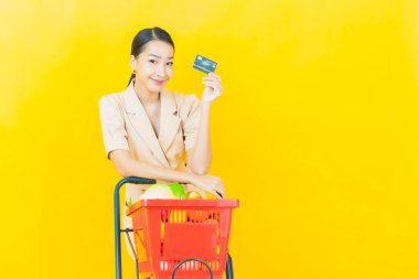 Renkli arka planda süpermarketten alınmış market sepetiyle gülümseyen güzel Asyalı kadın portresi.