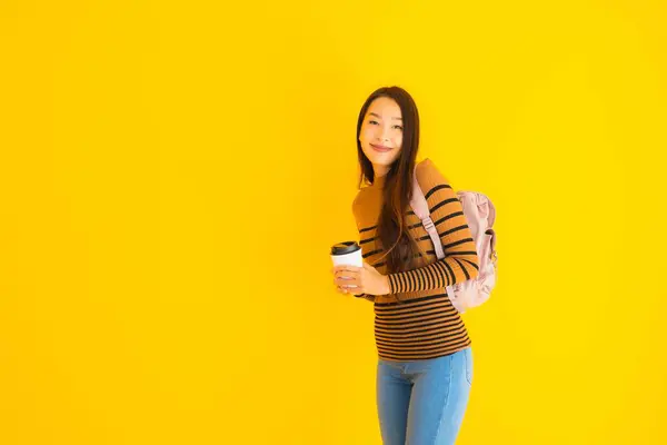 亚洲年轻貌美的女人 手里拿着旅行袋和咖啡杯 背景是黄色孤立的 — 图库照片