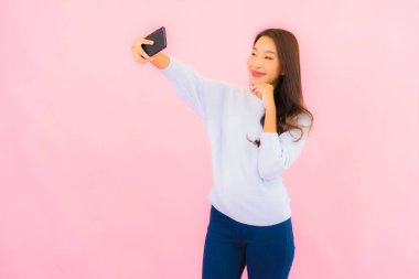 Portrait beautiful young asian woman use smart mobile phone on pink color isolated background