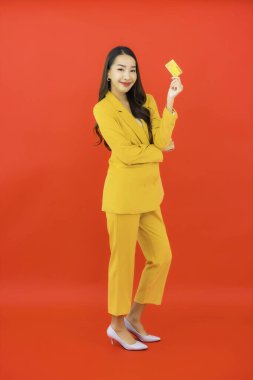 Güzel bir Asyalı kadının portresi kırmızı arka planda kredi kartıyla cep telefonu kullanıyor.