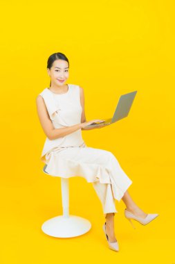 Asyalı güzel bir kadının portresi. Sarı izole edilmiş arka planda dizüstü bilgisayarla gülümsüyor.