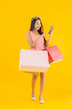 Renkli alışveriş çantalı güzel Asyalı kadın akıllı cep telefonu ve sarı izole edilmiş arka planda kredi kartı.