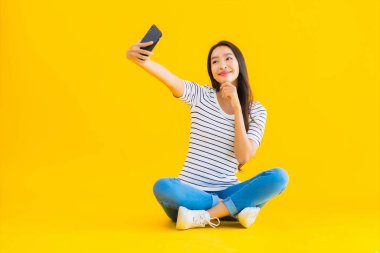 Güzel Asyalı genç bir kadının portresi mutlu bir gülümseme sarı izole edilmiş arka planda akıllı cep telefonu kullanın