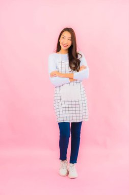 Portrait beautiful young asian woman in kitchen wear with apron on pink isolated background