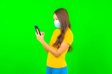 Güzel Asyalı genç bir kadının portresi, yeşil yalıtılmış arka planda kovid19 veya koronavirüsten korunmak için maske takar.
