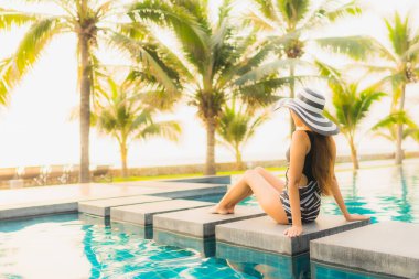 Güzel bir Asyalı kadın portresi, gün batımında palmiye ağacıyla birlikte havuz kenarında dinleniyor ya da tatil için gün doğumunda dinleniyor.