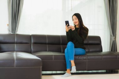 Güzel bir Asyalı kadın oturma odasındaki koltukta akıllı cep telefonu ya da cep telefonu kullanıyor.