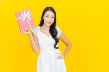 Asyalı güzel bir kadının portresi. Sarı arka planda kırmızı hediye kutusuyla gülümsüyor.