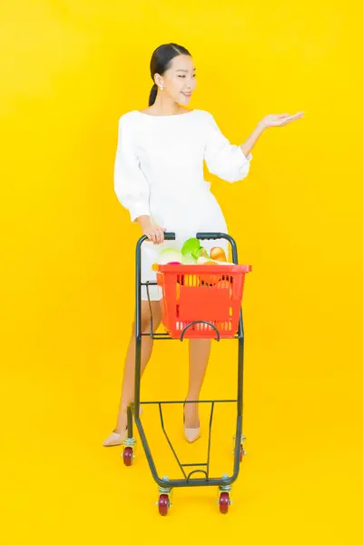 肖像画美しい若いアジアの女性は色の背景にスーパーマーケットからの食料品バスケットと笑顔 — ストック写真