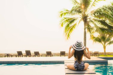 Güzel bir Asyalı kadın portresi, gün batımında palmiye ağacıyla birlikte havuz kenarında dinleniyor ya da tatil için gün doğumunda dinleniyor.