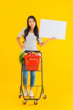 Market sepeti taşıyan güzel Asyalı kadın portresi ve sarı izole edilmiş arka planda beyaz boş tahta.