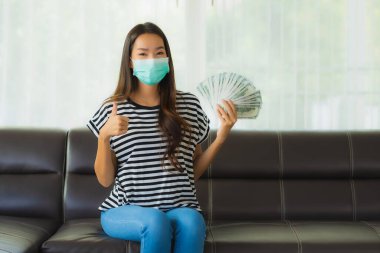 Maskeli güzel Asyalı kadının portresi evde para ya da para gösteriyor.
