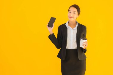 Portre güzel genç Asyalı kadın akıllı cep telefonu ve kahve fincanı ile izole edilmiş sarı arka planda