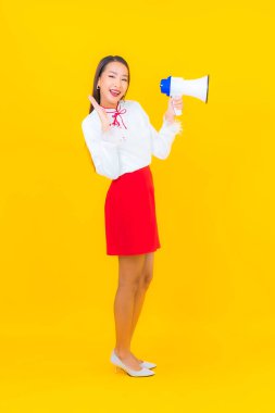 Güzel bir Asyalı kadın portresi sarı arka planda megafon kullanıyor.