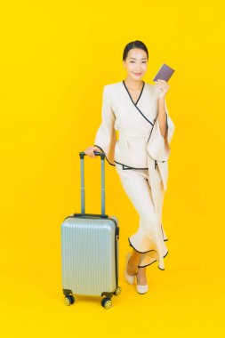 Güzel, genç, iş kadını, bavul ve pasaportlu Asyalı kadın, sarı arka planda seyahat etmeye hazır.