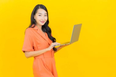 Asyalı güzel bir kadının portresi. Sarı izole edilmiş arka planda dizüstü bilgisayarla gülümsüyor.