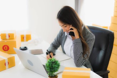 Güzel Asyalı iş kadını portresi evden bilgisayarlı cep telefonuyla karton kutuyla çevrimiçi alışveriş için hazır bekliyor.