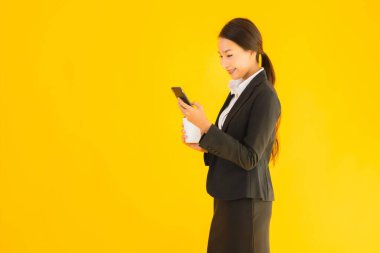 Portre güzel genç Asyalı kadın akıllı cep telefonu ve kahve fincanı ile izole edilmiş sarı arka planda
