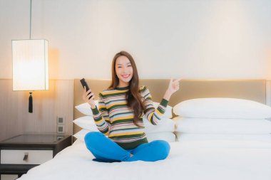 Güzel bir Asyalı kadın yatak odasının içinde akıllı cep telefonu kullanıyor.