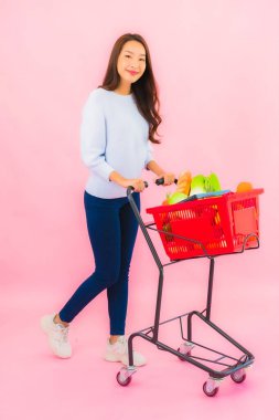 Portrait beautiful young asian woman with fruit vegetable and grocery in basket on pink isolated background