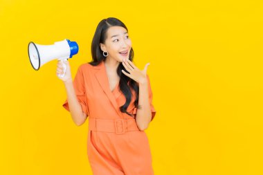 Asyalı güzel bir kadının portresi sarı arka planda megafonla gülümsüyor.