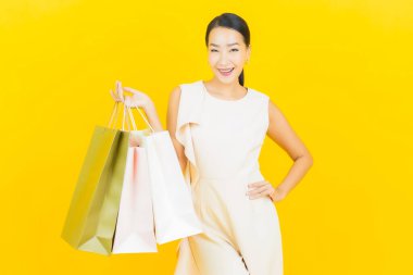 Sarı arka planda alışveriş çantasıyla gülümseyen güzel Asyalı kadın portresi